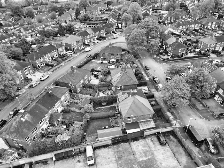An aerial view of a suburban residential area showcasing several well-maintained gardens with neatly trimmed lawns, hedges, and flower beds. The image features a variety of plants including mature tre